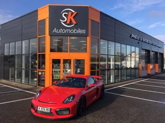Façade de SK Automobiles avec une voiture de sport rouge garée à l'avant.
